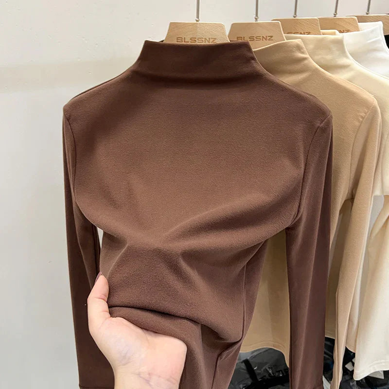 Hand holding soft brown turtleneck sweater on wooden BLSSNZ hanger with beige and white sweaters in background