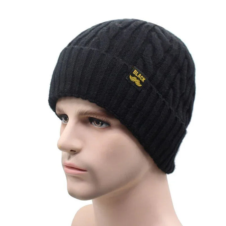 Black knitted beanie hat with cable pattern and small yellow logo on mannequin head