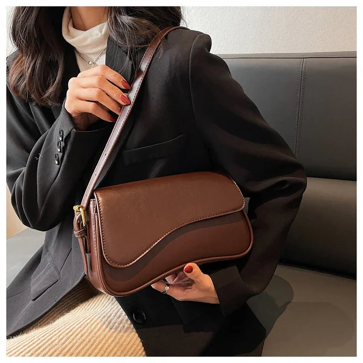 Woman wearing black blazer holding a brown leather shoulder bag with wavy flap design