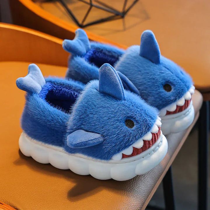 Blue fuzzy shark slippers with white teeth and angry eyes on a brown chair
