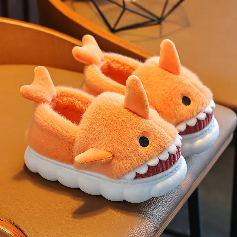 Cozy orange plush shark slippers with white teeth and fins on white soles, placed on a brown surface