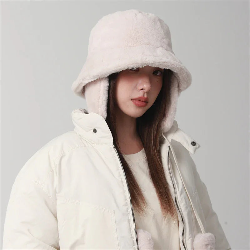 Woman wearing a white fluffy bucket hat and a white puffer jacket against a plain background