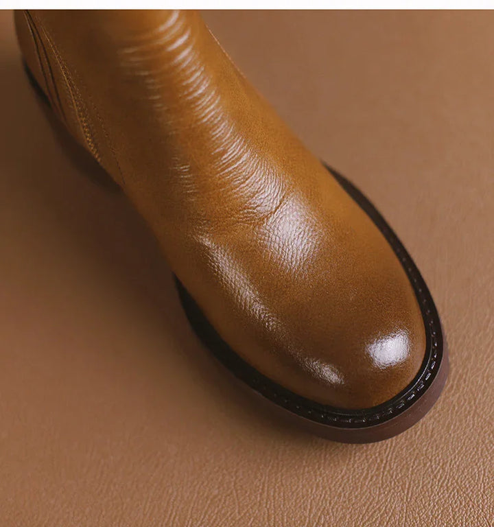 close-up of polished tan leather boot toe with dark sole on matching brown surface