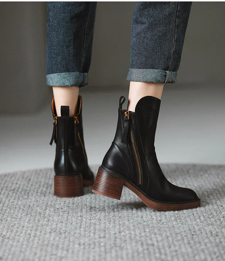 Black leather ankle boots with brown stacked heels and side zippers worn with cuffed blue jeans on gray carpet