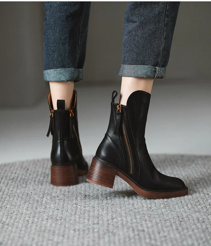 Black leather ankle boots with brown stacked heels and side zippers worn with cuffed blue jeans on gray carpet