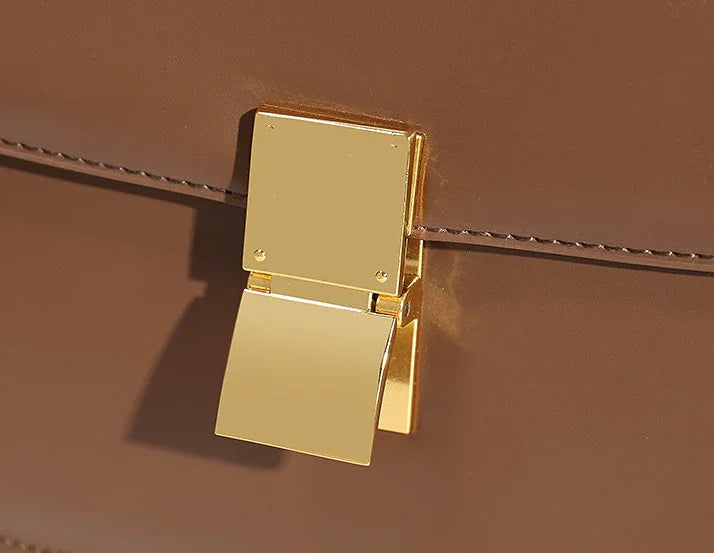Close-up of gold metal clasp on brown leather handbag with stitched detail