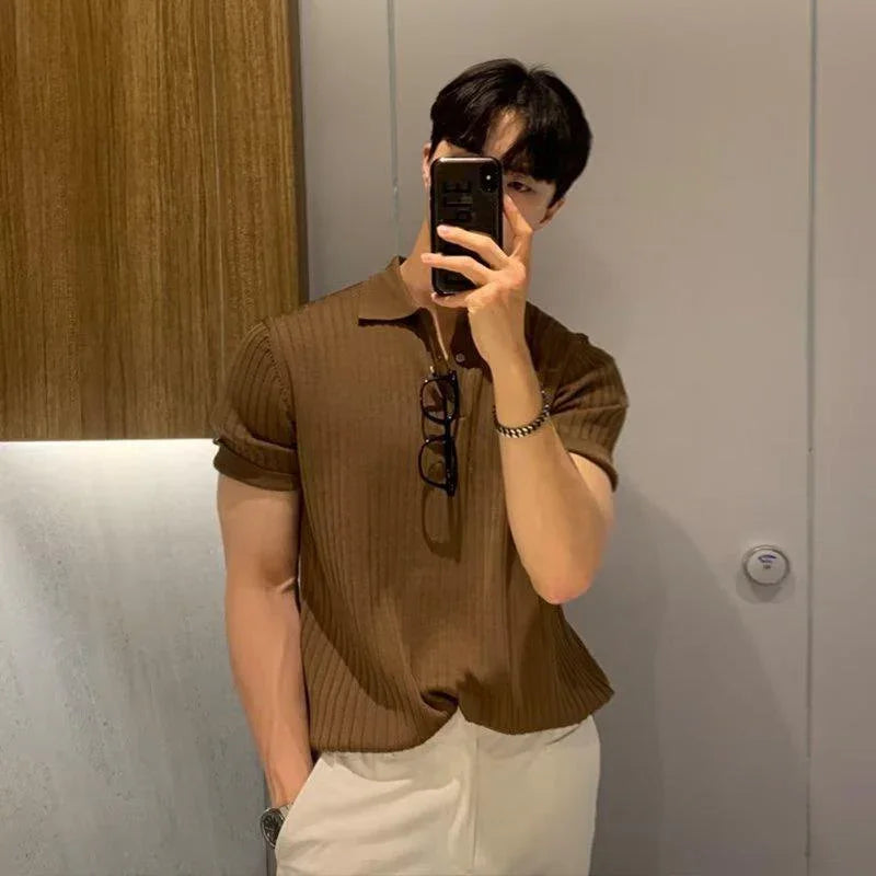 Man taking mirror selfie wearing brown ribbed polo shirt and beige pants with glasses hanging on shirt