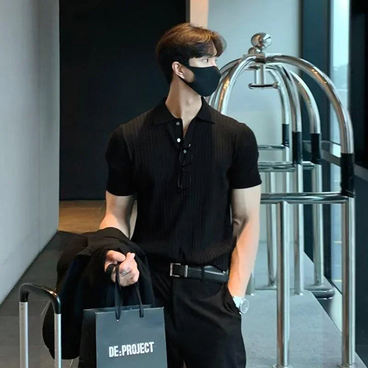 Man in black polo shirt and mask holding DE:PROJECT shopping bag near luggage cart in modern hotel lobby