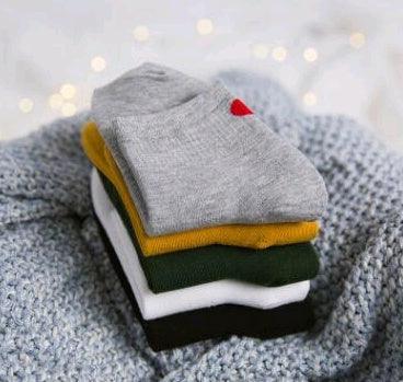 Stack of folded colorful socks including gray with red heart on knitted gray blanket with bokeh lights