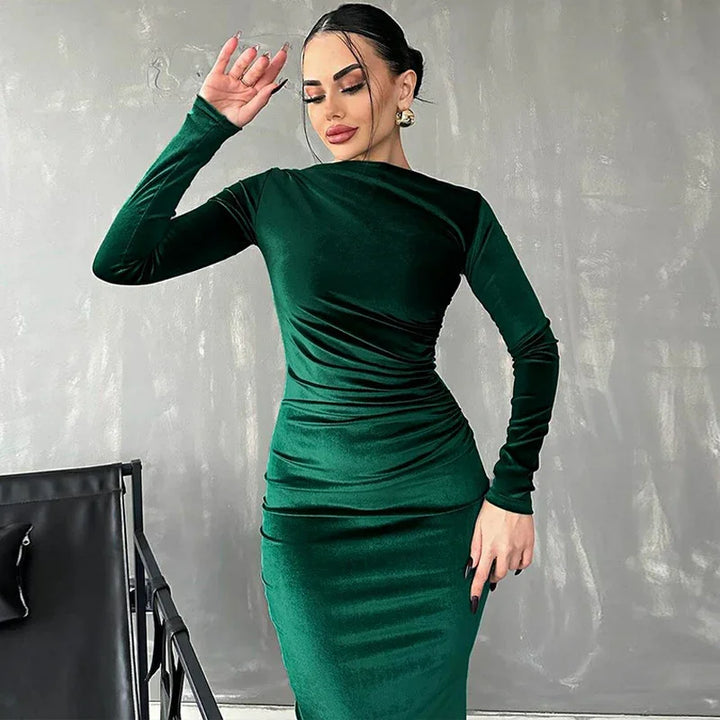 elegant woman posing in a fitted long sleeve dark green velvet dress against a gray textured wall