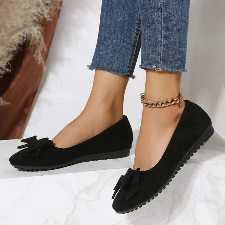Woman wearing black suede ballet flats with bow detail and gold chain anklet with blue jeans
