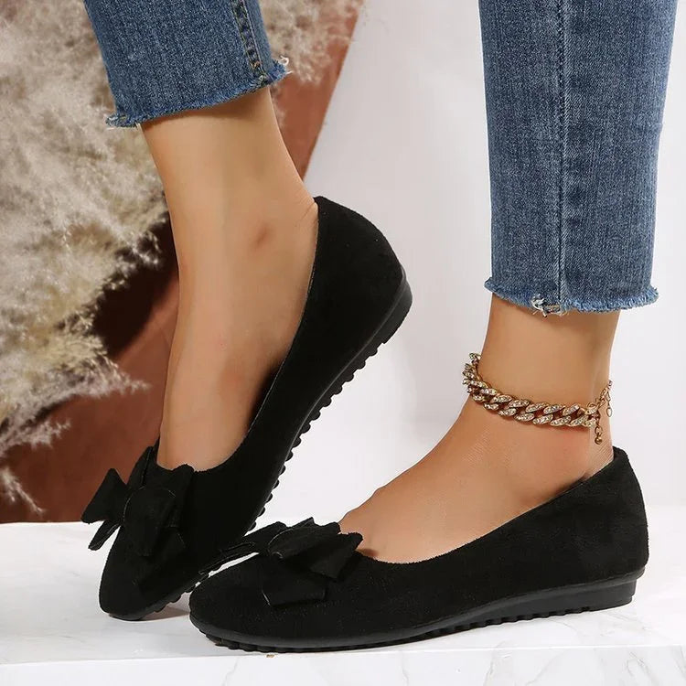 Black suede flat shoes with bow details worn with gold anklet and frayed hem blue jeans