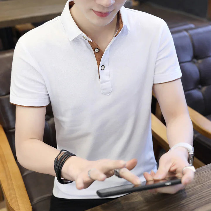 Man wearing white short-sleeve polo shirt with brown button placket using smartphone indoors