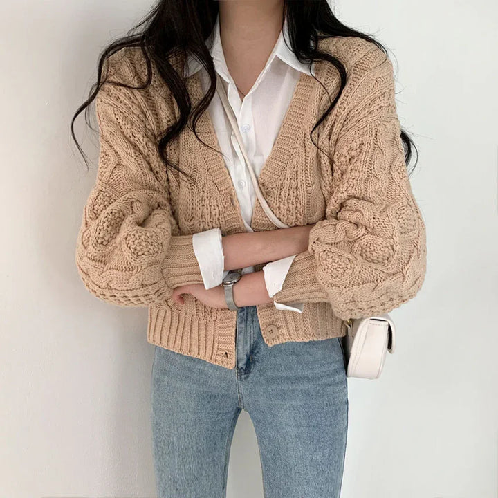 Woman wearing beige chunky knit cardigan over white shirt and light blue jeans with white crossbody bag