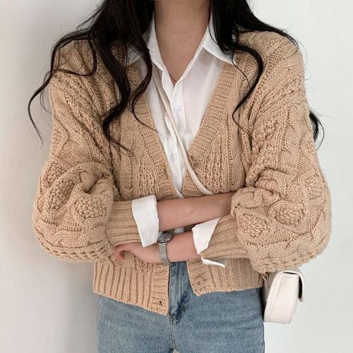 Woman wearing beige chunky knit cardigan over white shirt and blue jeans with a white purse