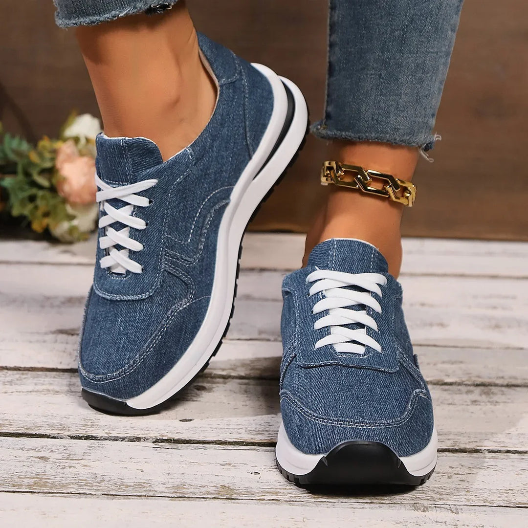 Denim sneakers with white laces worn with rolled jeans and gold chain anklet on wooden floor