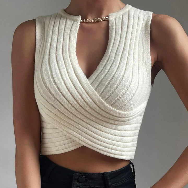 Woman wearing a white ribbed knit sleeveless crop top with gold chain detail and black pants