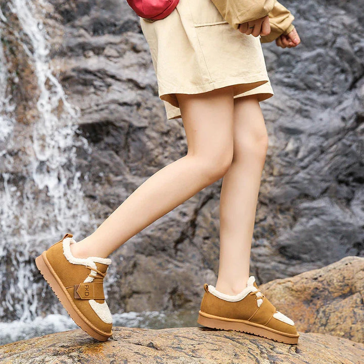 Person wearing brown winter shoes with fur lining walking on rocky terrain near waterfall