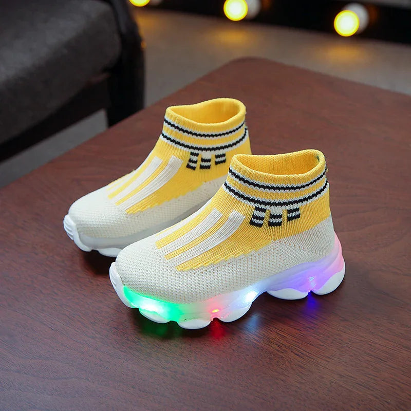 Kids yellow and white light-up sock sneakers with striped ankle cuff on wooden surface