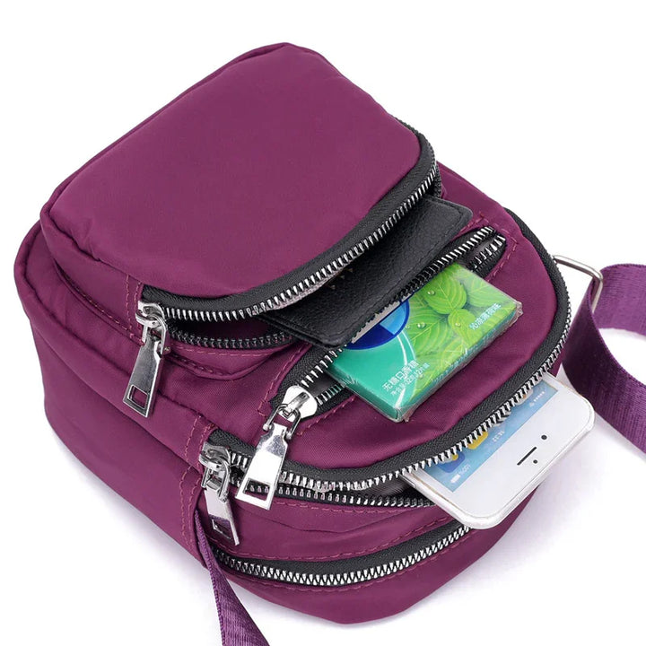 Compact purple crossbody bag with multiple zippered compartments, holding a smartphone and green pack