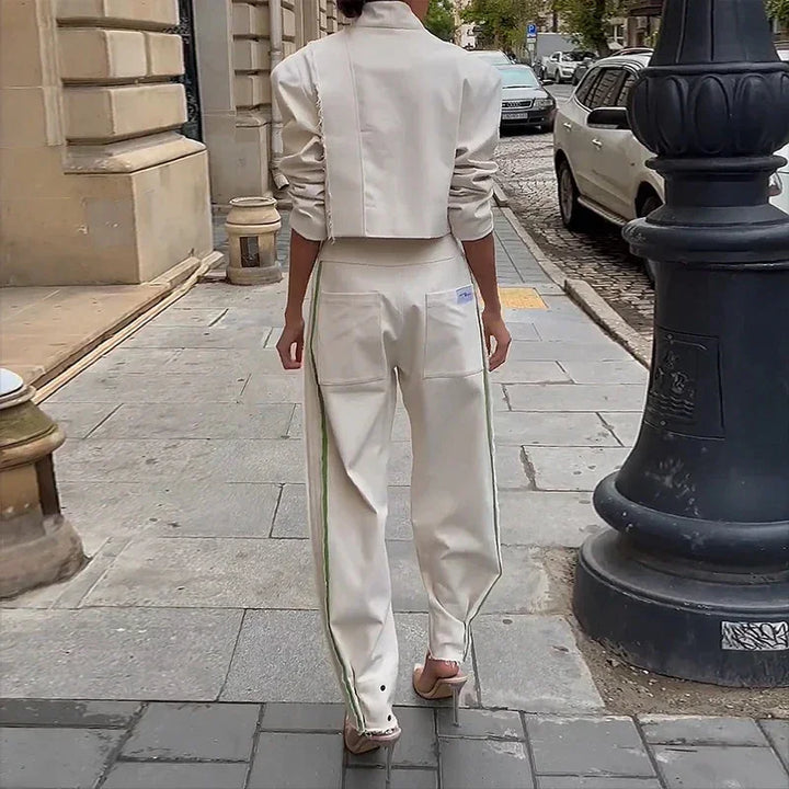 Woman walking on city sidewalk wearing white cropped jacket and wide-leg pants with green side stripes
