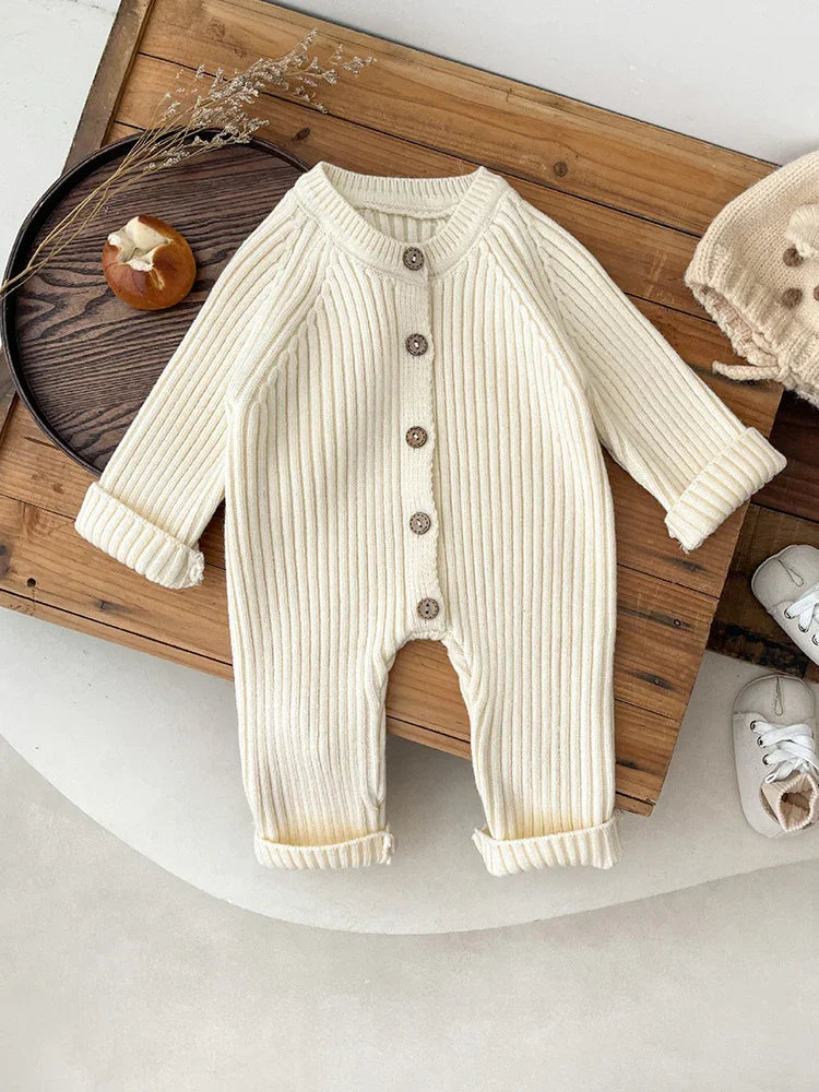 Cream ribbed knit baby onesie with wooden buttons on wooden tray, cozy infant outfit