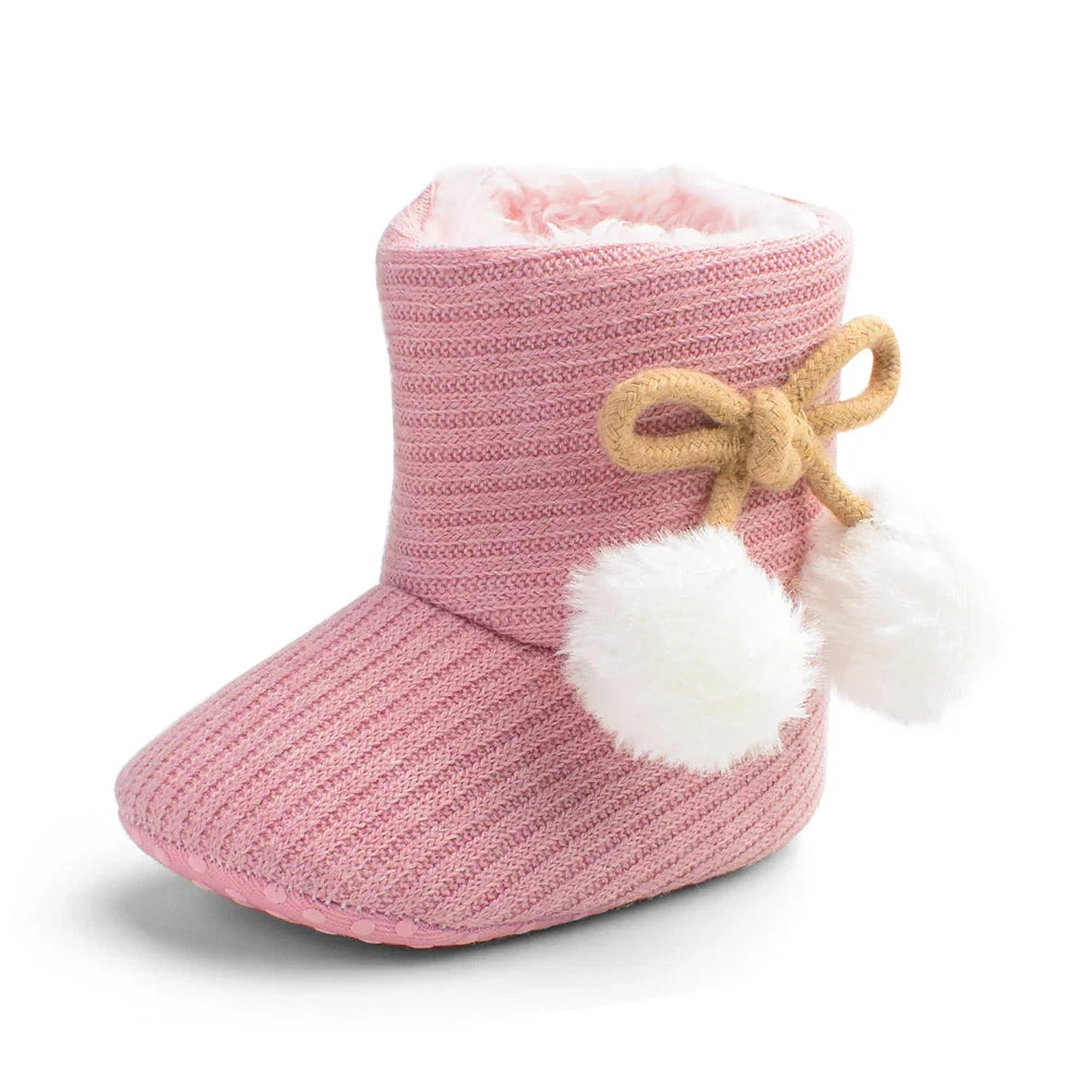 Pink knitted baby bootie slipper with soft white fur lining and pom-pom bow detail