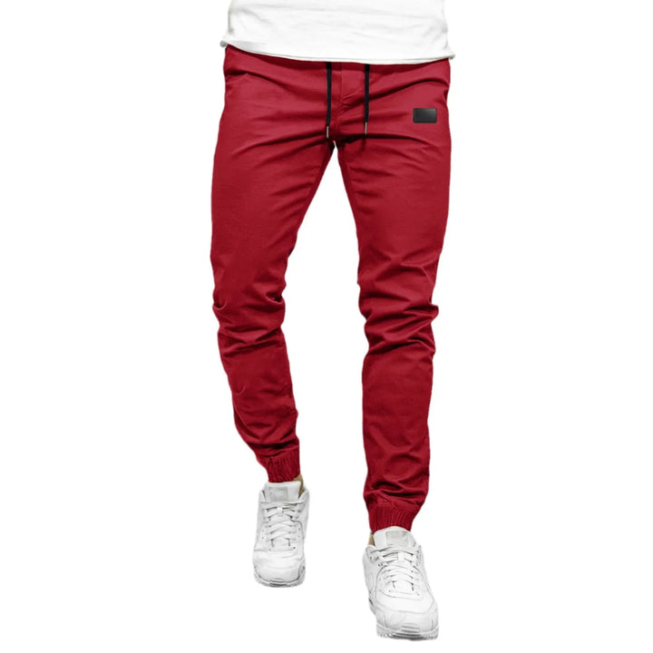 Men's slim fit red jogger pants with elastic cuffs and black drawstring worn with white sneakers