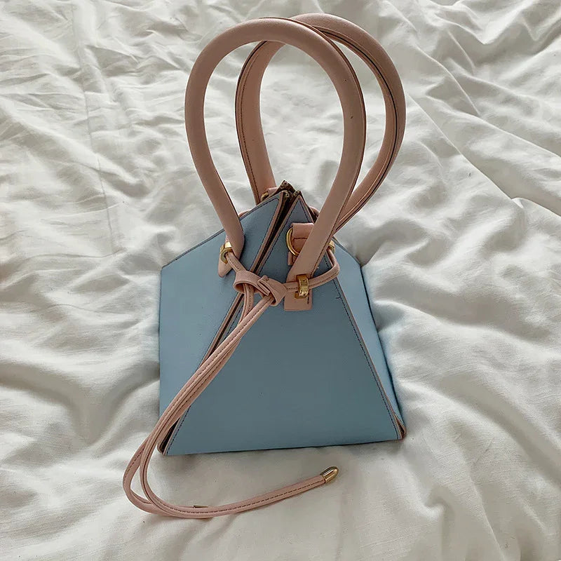 Light blue triangular leather handbag with beige handles and gold hardware on white fabric