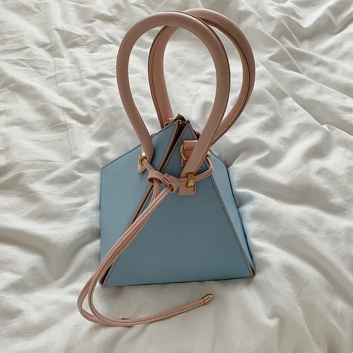 Light blue triangular leather handbag with beige handles and gold hardware on white fabric