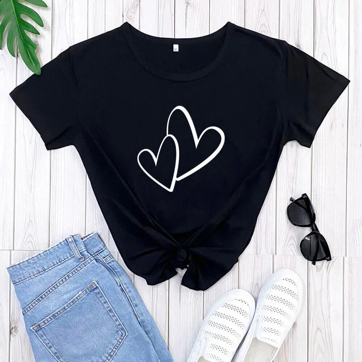 Black t-shirt with white double heart design, paired with blue jeans, white shoes, and black sunglasses on white wooden floor
