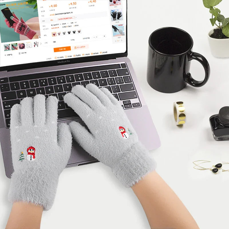 Hands wearing soft gray winter gloves with snowman embroidery typing on a laptop keyboard