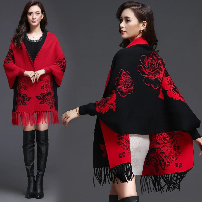 Woman wearing red and black floral patterned fringed shawl with black over-the-knee boots on gray background