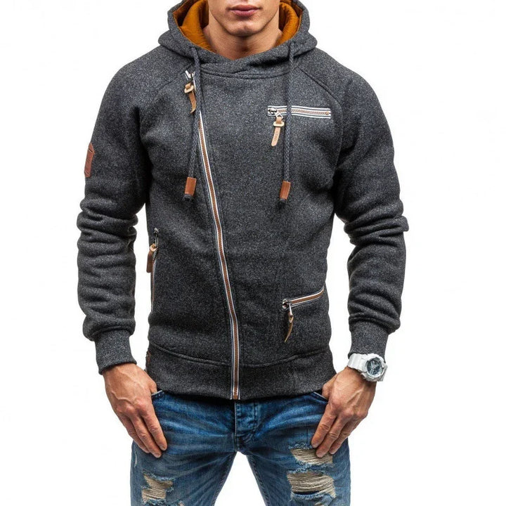 Man wearing dark gray asymmetrical zip hoodie with brown accents and ripped blue jeans