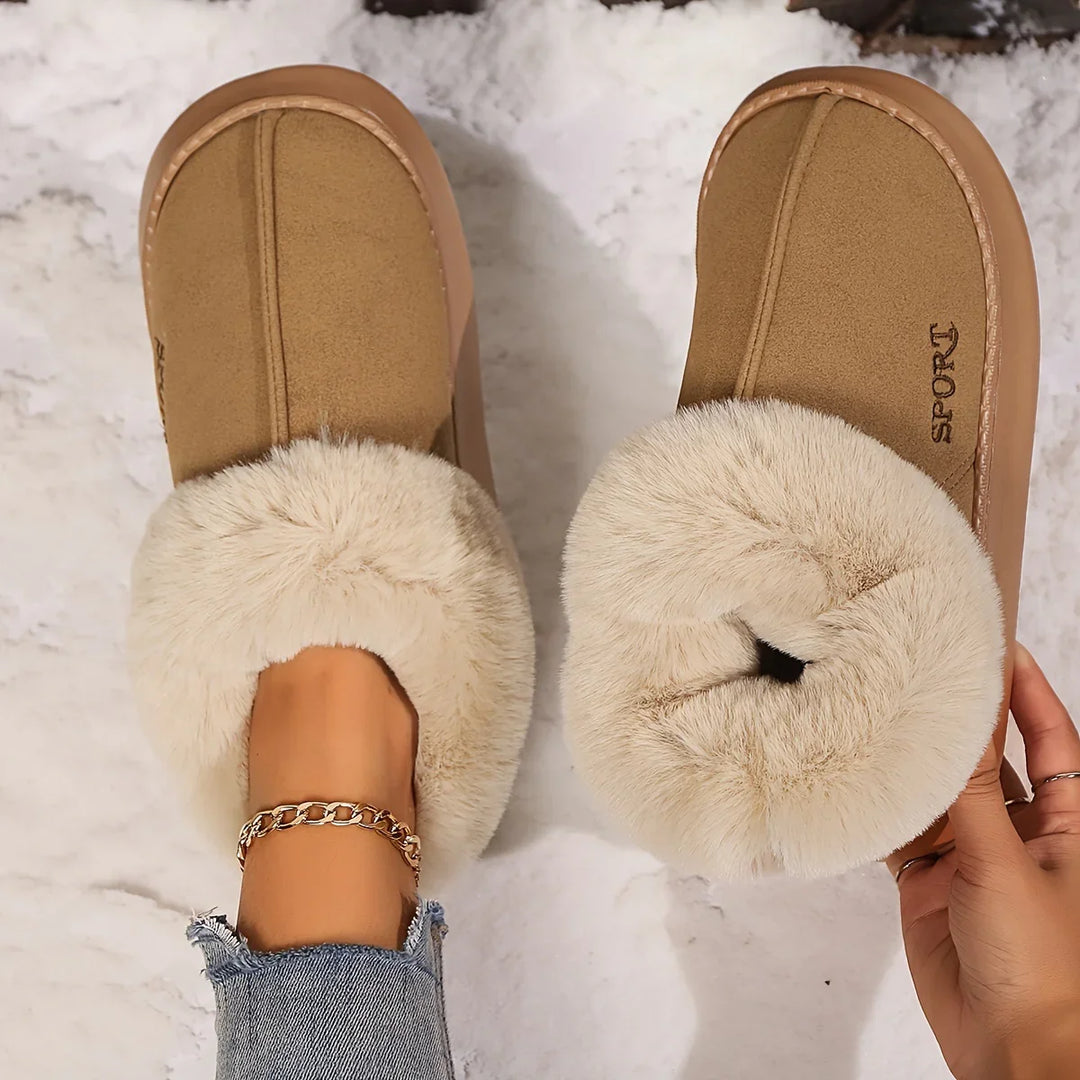 Tan cozy slip-on slippers with plush cream fur lining on snowy white surface