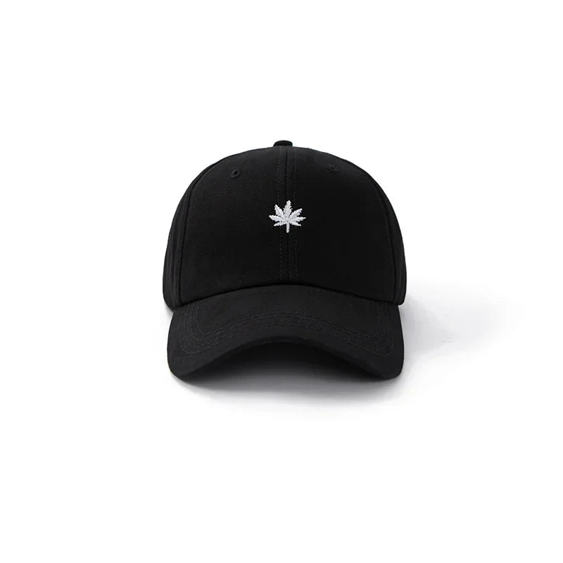 Black baseball cap with white embroidered marijuana leaf logo on front, isolated on white background