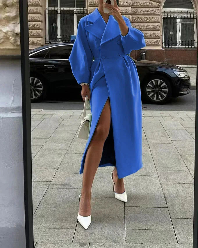 Woman in a bright blue long coat with puff sleeves and thigh slit, wearing white heels and carrying white handbag, urban street background