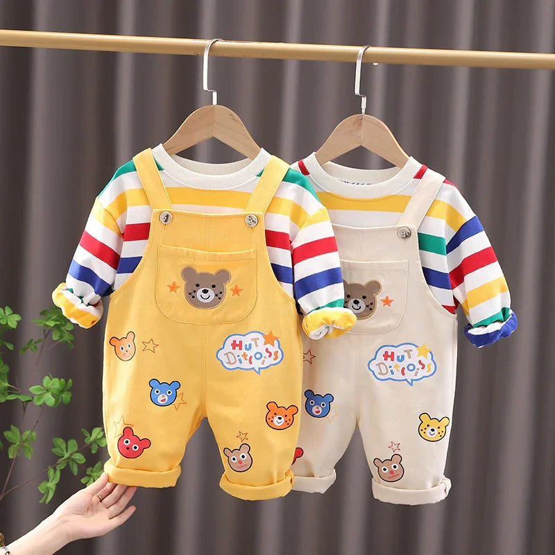 Two baby overalls with colorful bear prints paired with striped long-sleeve shirts hanging on wooden hangers