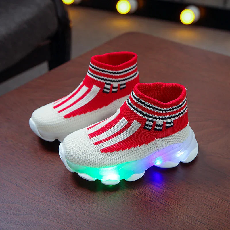 Red and white kids' LED light-up sock sneakers on wooden table with colorful glowing soles