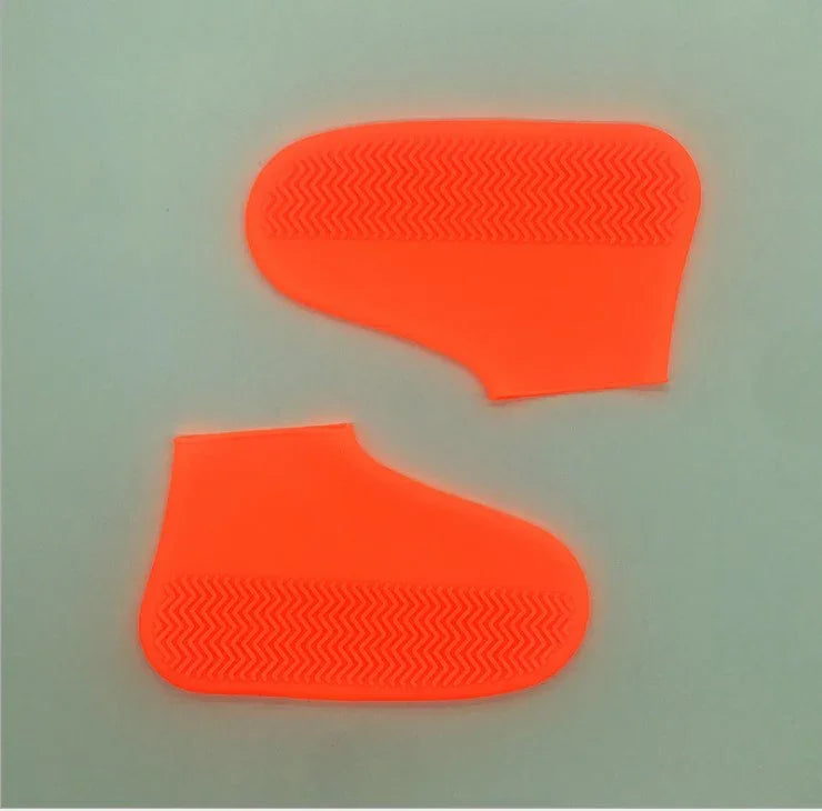 Pair of bright orange silicone shoe covers with textured sole pattern on gray background