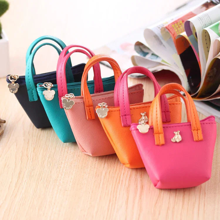 Row of five colorful small tote bags in pink, orange, beige, teal, and black on wooden surface