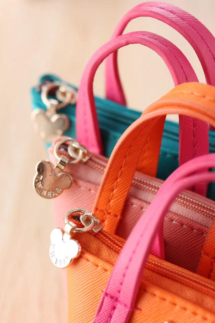 Close-up of colorful mini handbags with pink and orange handles and Mickey mouse-shaped zipper pulls
