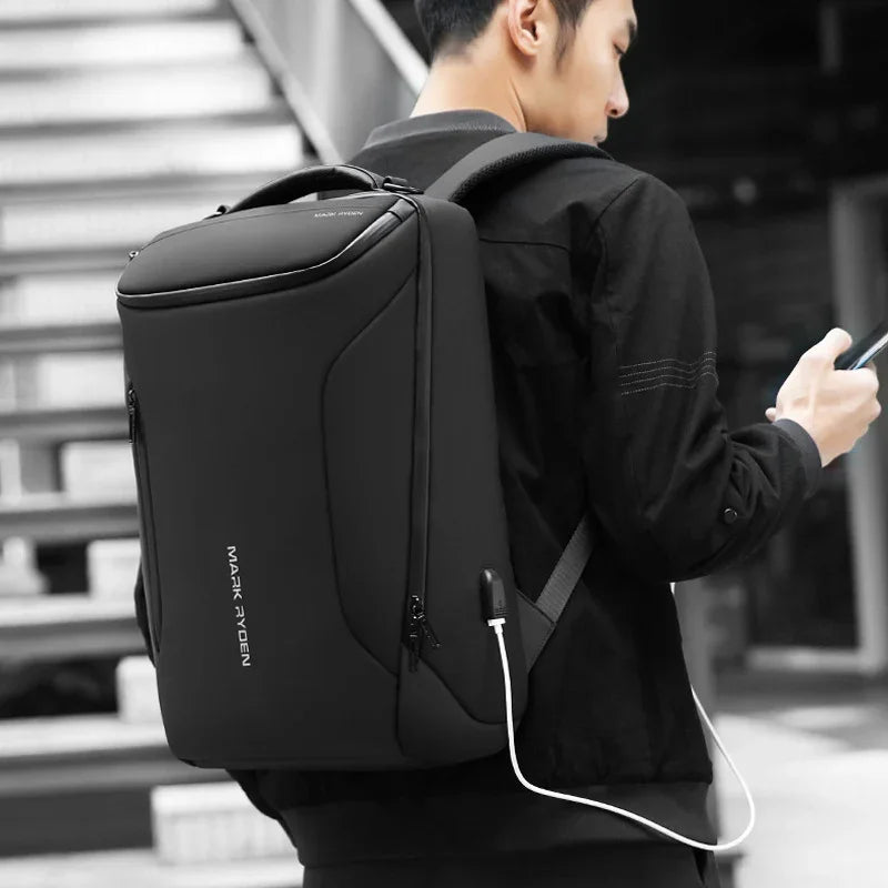 Man wearing sleek black Mark Ryden backpack with USB charging port, holding smartphone outdoors