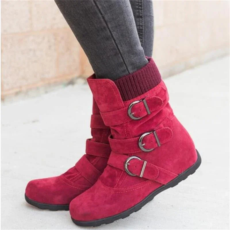 Close-up of red suede ankle boots with triple buckle straps and black soles worn with dark jeans