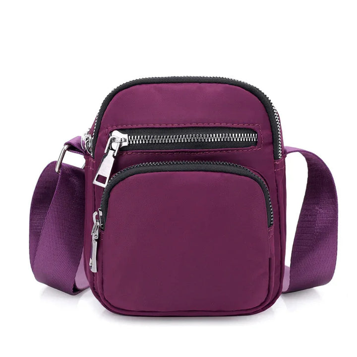 Small purple crossbody bag with front zippered pockets and adjustable strap