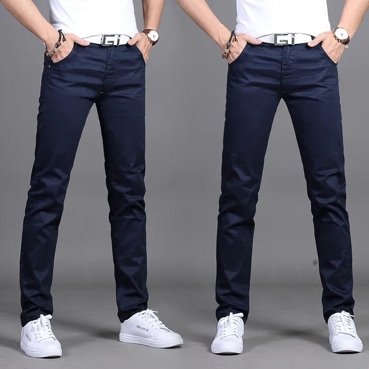 Front view of man wearing slim fit navy blue pants with white belt, white sneakers, and white shirt