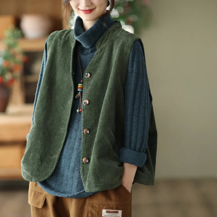 Woman wearing green corduroy vest over blue textured turtleneck and brown pants indoors
