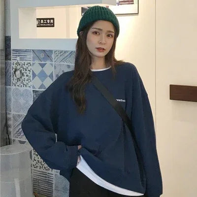 Young woman wearing a green knit beanie, navy blue oversized sweater, and casual black crossbody bag indoors