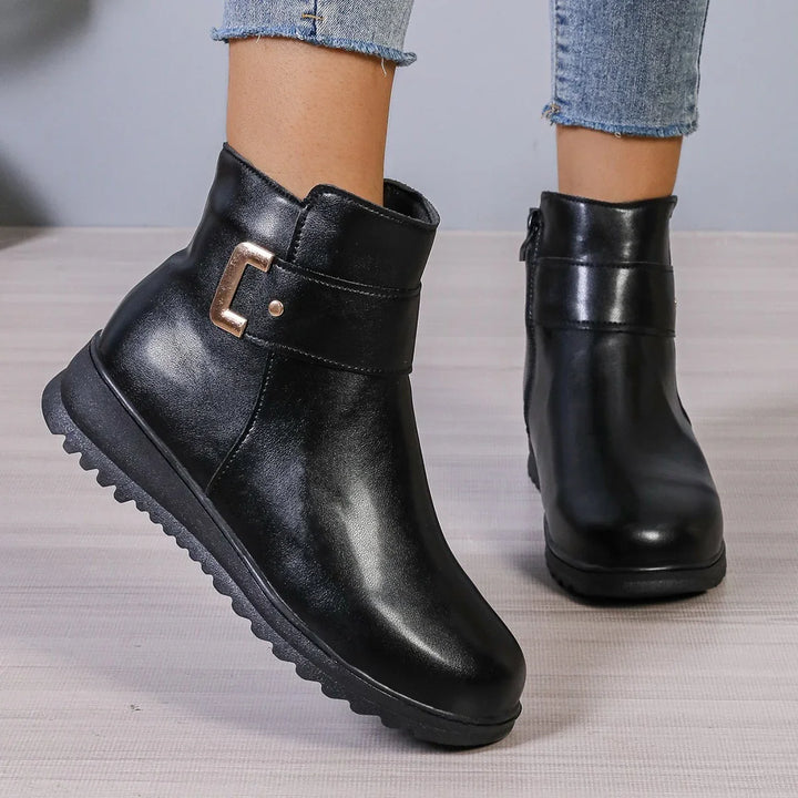 Black leather ankle boots with gold buckle detail worn with cropped blue jeans on wooden floor