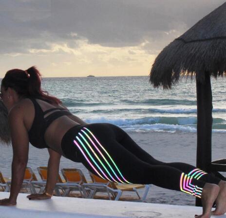 Woman in black workout clothes doing plank exercise on beach with ocean and lounge chairs